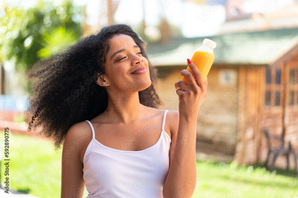 Young African American woman holding an orange juice at outdoors Young African American woman holding an orange juice at outdoors