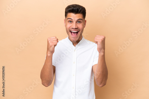 Young caucasian man isolated on beige background celebrating a victory in winner position © luismolinero