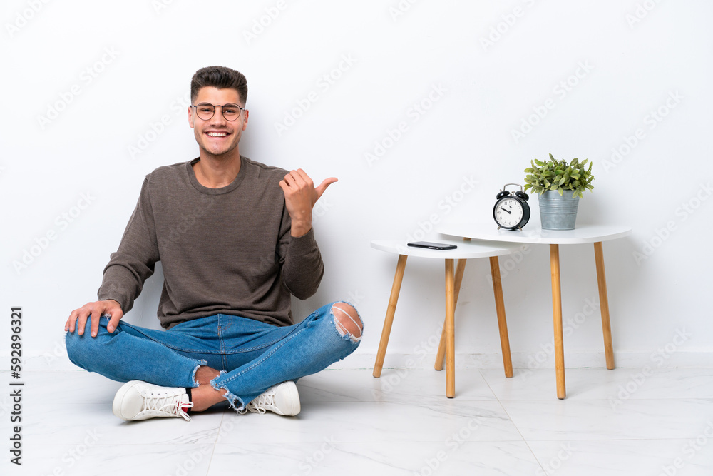 Young caucasian man sitting in his home isolated on white background pointing to the side to present a product