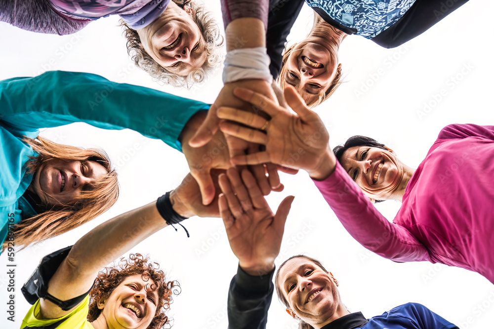 Obraz premium Happy multigenerational women stacking hands together after sport workout outdoor - Female friends having fun together and putting their hands on top of each other - Bright filter with shot from below