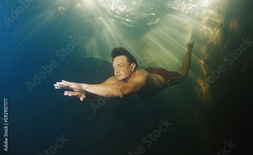 Man dives in the freshwater river with sunny rays shining through the water