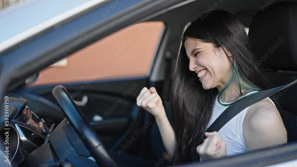 Young beautiful hispanic woman sitting on car doing winner expression at street Young beautiful hispanic woman sitting on car doing winner expression at street