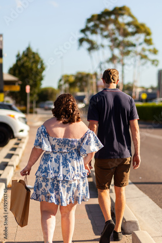 Sunlit young person carrying brown paper shopping bag walking down footpath in community photo