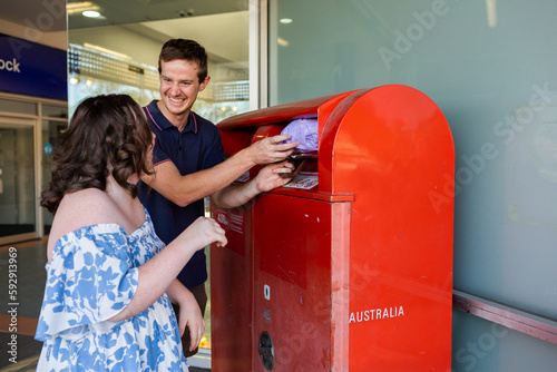 Happy teenager with down syndrome using post office box to send parcel in compostable packaging photo