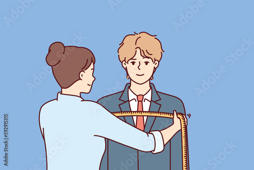 Woman tailor measures shoulders of man in centimeters to make formal suit to individual measurements. Guy at reception at tailor making handmade clothes according to individual sketches 