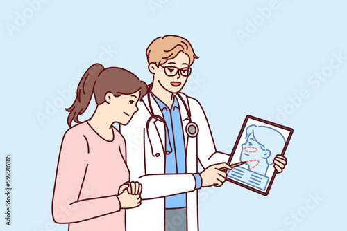 Man plastic surgeon consults woman patient demonstrating tablet with ways to tighten skin on face to get rid of wrinkles. Girl turned to plastic surgeon for help to do facial surgery 