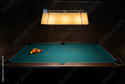 Regular footage of a billiard table in a dark room with colorful balls on it and a lamp above