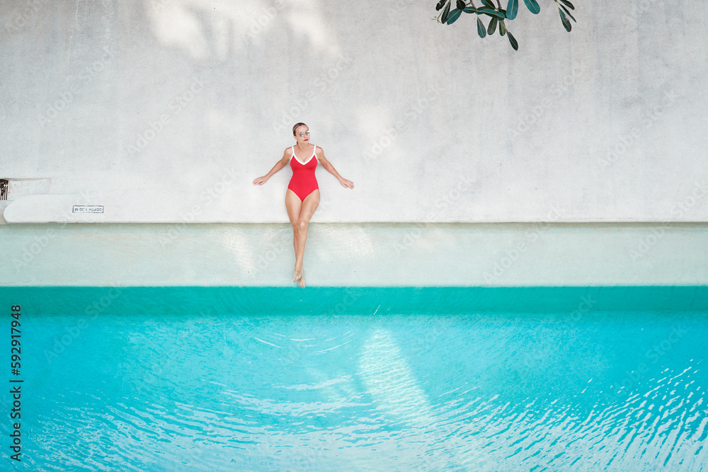 Enjoying suntan and vacation. Top view of pretty young woman in red swimsuit lying near swimming pool.