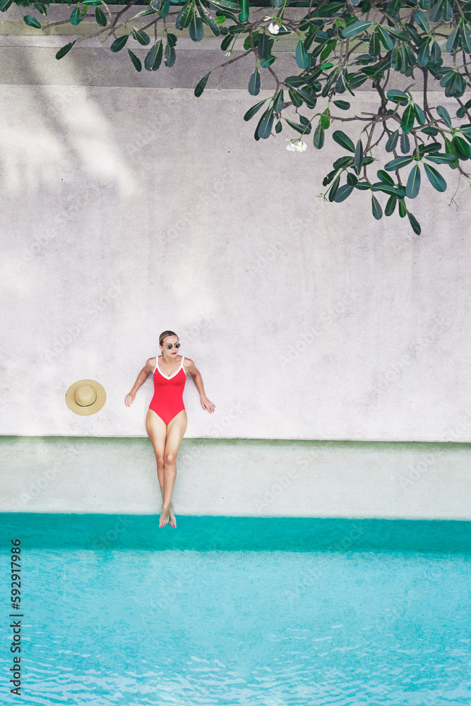 Enjoying suntan and vacation. Top view of pretty young woman in red swimsuit lying near swimming pool.