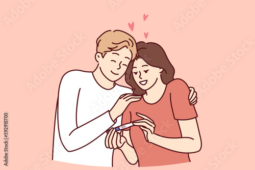 Happy couple with pregnancy test rejoices to see result predicting birth of child. Man and woman hugging in love looking at pregnancy test after successful conception for family planning concept 