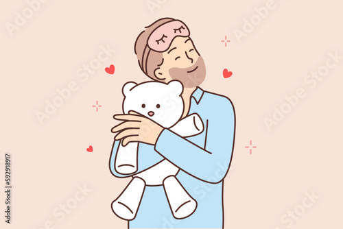 Funny bearded man hugging teddy bear before going to bed feeling attached to gift toy