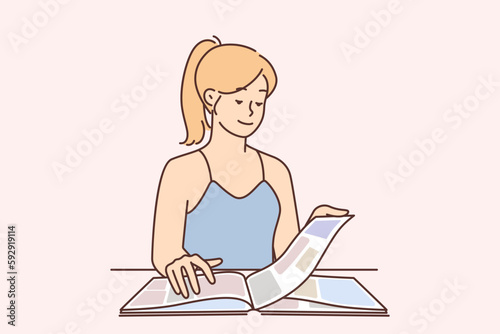Carefree young woman reading magazine and flipping through page with photos or news about celebrity