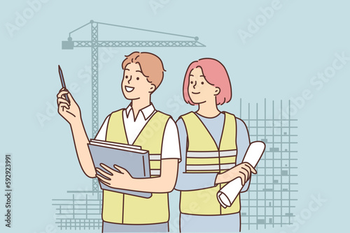 Man and woman in construction uniforms inspect construction site with unfinished high-rise buildings