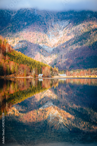 Fototapeta Naklejka Na Ścianę i Meble -  Vertical shot of a lake reflecting the colors of autumn trees and a high mountain covered in fog