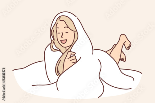 Laughing woman wrapped in blanket lies on bed not wanting to get up and go to work or college