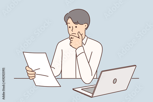Embarrassed businessman with documents from bank or tax office sitting at table with laptop 