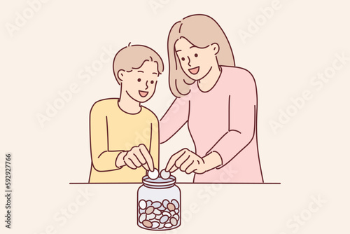Mom and son together throw coins into moneybox, wanting to save up money for cherished wish photo