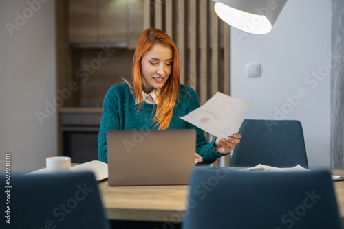 Young businesswoman working at home with laptop and some documents on desk