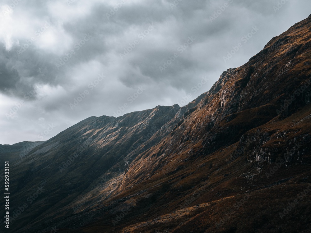 Horizontal view of the rocky mountains of Glencoe, Scottland under a clouded gray sky