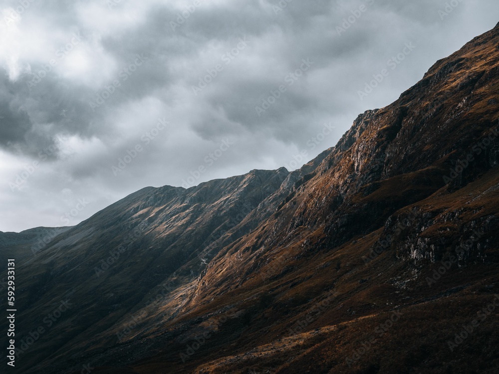 Fototapeta premium Horizontal view of the rocky mountains of Glencoe, Scottland under a clouded gray sky