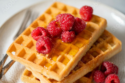 Closeup waffles with berries in plate served with cup of tea.