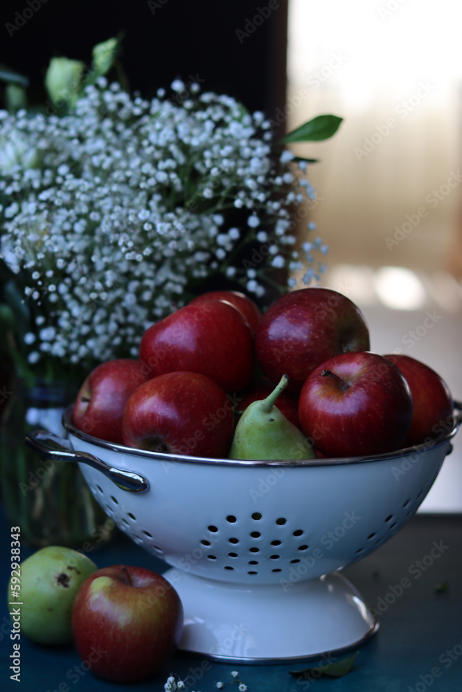 Red apples on black background. Vibrant colors of fresh seasonal fruit. Apples in a colander. White flowers and fruit still life. 