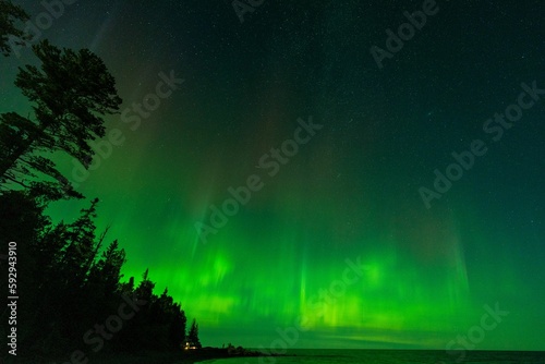 Aurora borealis over the lake surrounded by forest in Keweenaw Peninsula  Michigan