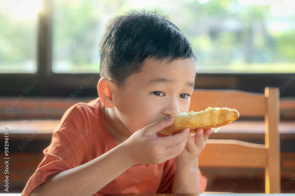 Asian boy eating sweet croissant in restaurant with beverage Asian boy eating sweet croissant in restaurant with beverage