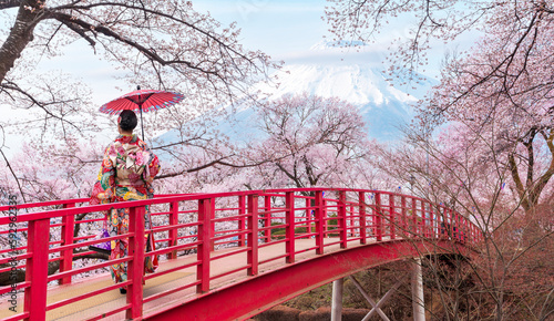 Woman traveller with a red umbrella and walking over the bridge with Fuji mountain and Sakura flower background
