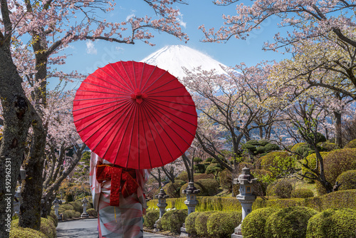 Asian traveller woman in traditional kimono dress and red umbrella walking with Fuji mountain with cherry blossom flower background