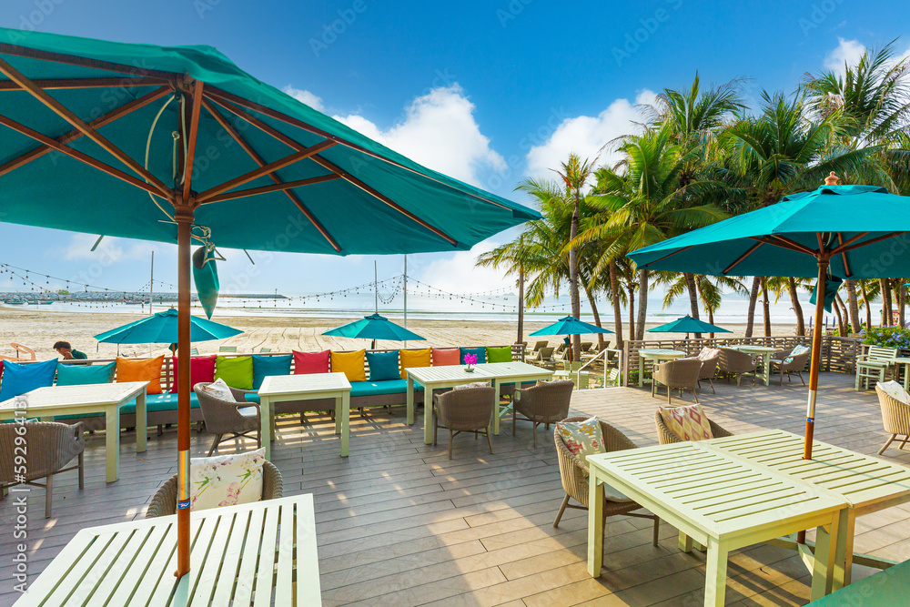 Seaside restaurant,Beach club concept, food corner or cafe, restaurant tables, straw natural chairs, wooden tables, makrome knitted sun umbrellas, white modern sun beds, sea view on background