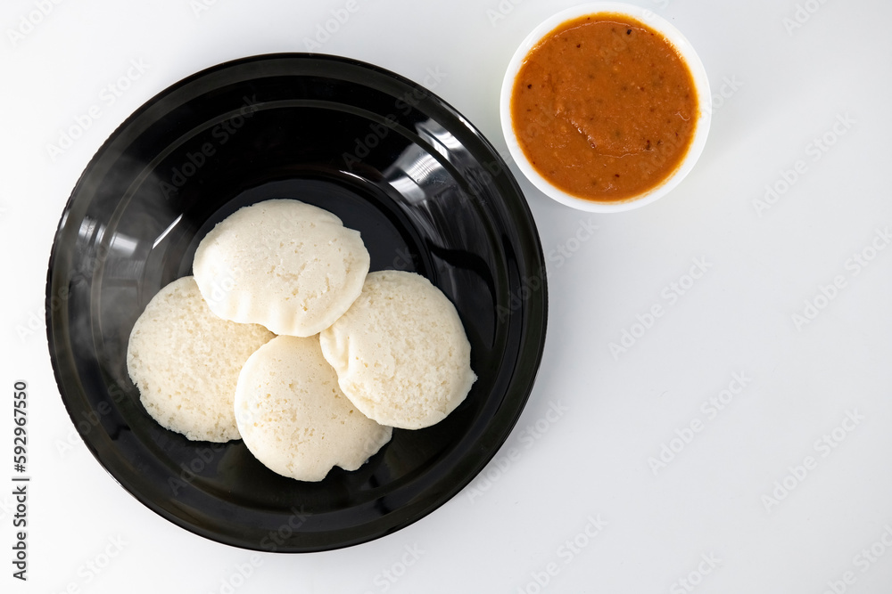 Hot and steaming idly in a black plate and tomato chutney in a isolated white background. Steaming hot idly and red chutny isolated. Healthy food / Break fast in india.