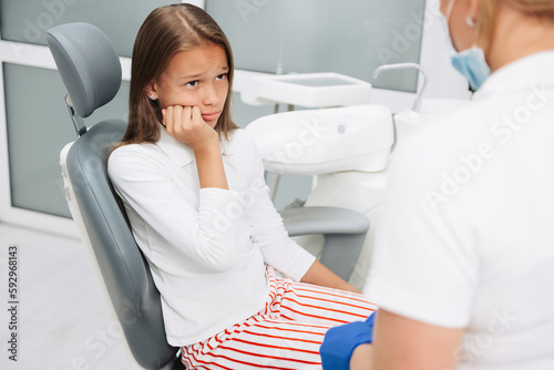 Adorable little girl having toothache looking sad sitting in a dental chair visiting dentist.