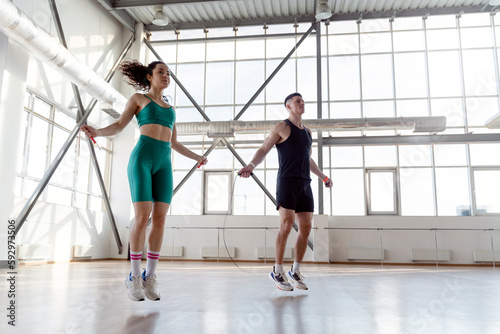 Sporty couple, man and woman training in gym, jumping rope. Attractive people take care of health