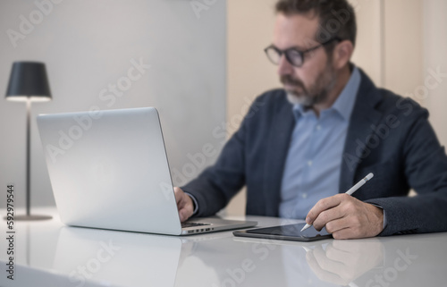 Businessman working with laptop and tablet sitting at the desk. Man write with electronic stylus pen