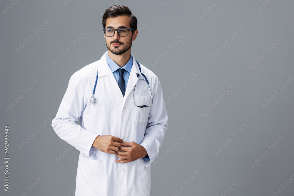 A serious doctor man in a white coat and eyeglasses and a stethoscope looks at the camera on a gray isolated background, copy space, space for text, health A serious doctor man in a white coat and eyeglasses and a stethoscope looks at the camera on a gray isolated background, copy space, space for text, health