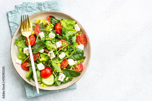 Spring salad in craft plate. Spinach, arugula, tomatoes and feta with olive oil. Top view on white.