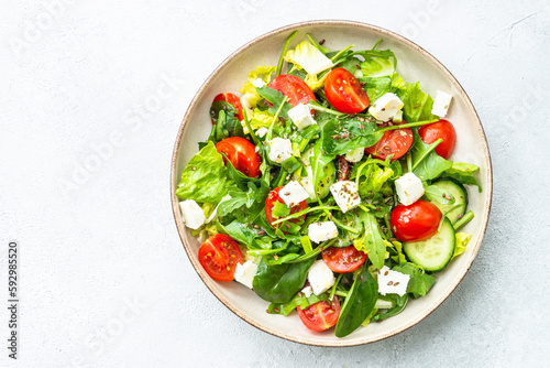 Spring salad in craft plate. Spinach, arugula, tomatoes and feta with olive oil. Top view on white.