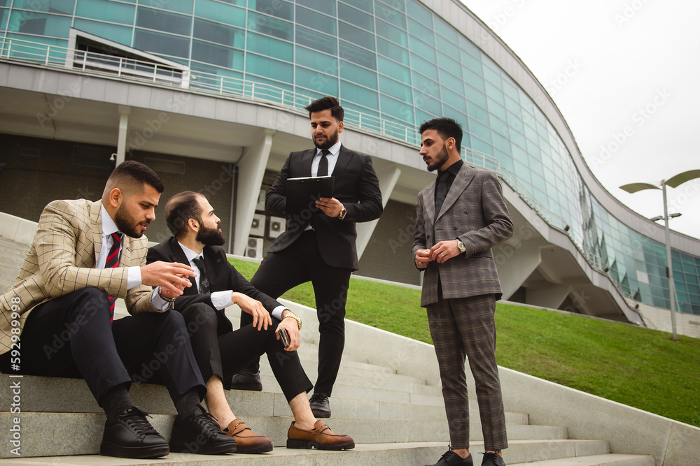 Fototapeta premium A group of business people meet outdoors. Male employees in suits communicate outdoors. Business partners discuss and argue. Relationships and promotion. Teamwork and friendship