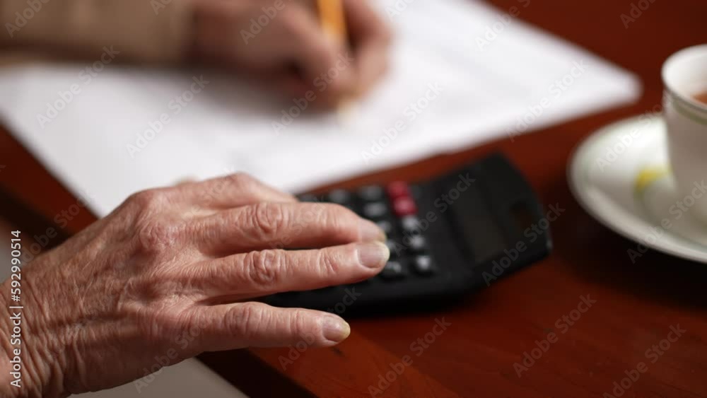 Adult senior elderly woman hands on calculator and paper documents at home. Old woman works on family budget, pension costs.