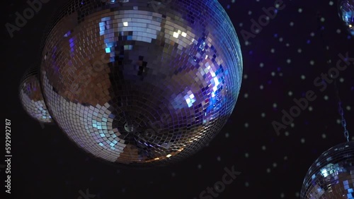 Silver mirror disco ball suspended from the ceiling rotates quickly, light spot rays and glare. White stage light at a concert hall, club, party or disco. Illumination and atmosphere. photo