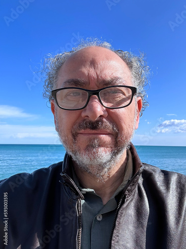 middle aged italian man with curly graying hair and glasses by the sea against the sky