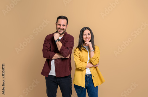 Portrait of cheerful attractive boyfriend and girlfriend dressed in casuals looking at camera. Smiling young couple touching chins and posing happily on isolated beige background photo