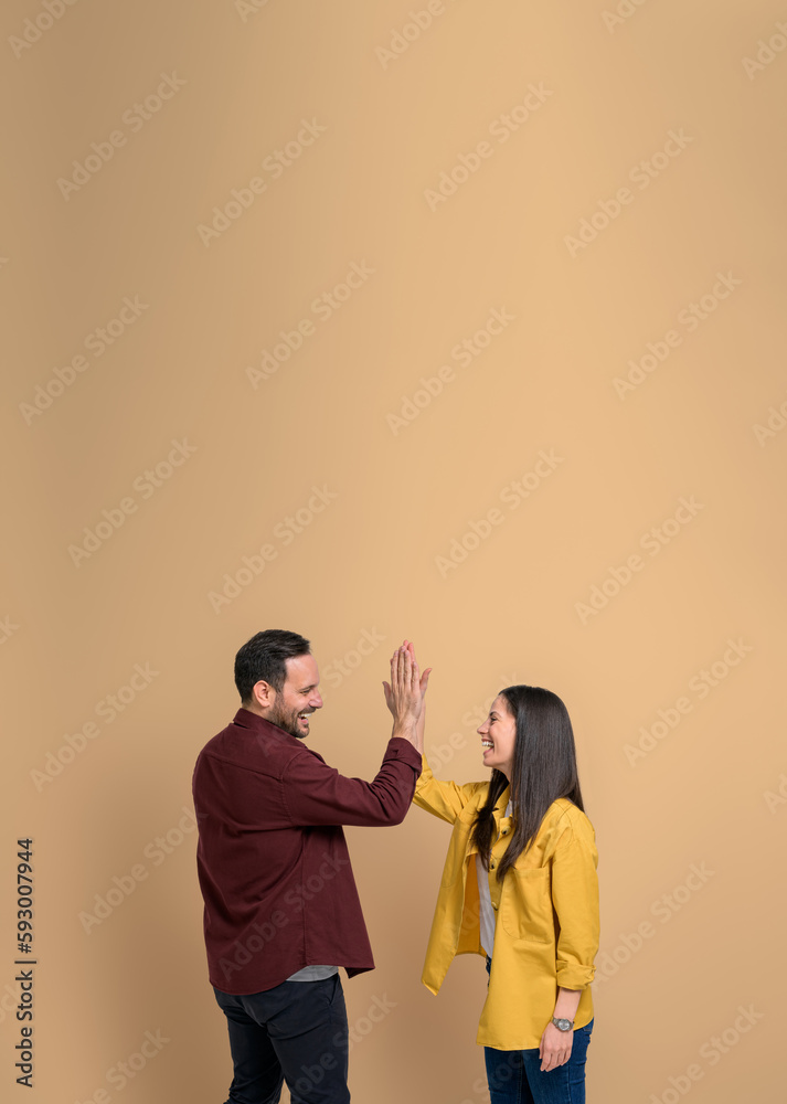 Side view of joyful man and woman giving high-five to each other and shouting against beige background. Excited loving couple clapping hands and greeting while celebrating victory and success