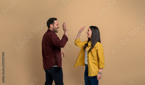 Canvastavla Side view of cheerful boyfriend and girlfriend giving high-five to each other and screaming over beige background