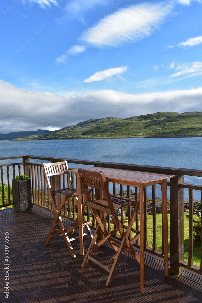 wooden brown bench and table stand outdoor at bacolny  over the sea of skye island  ,blue and white sky