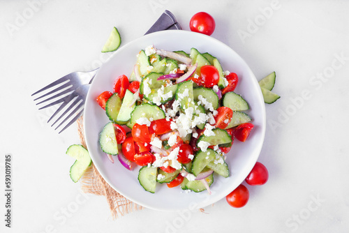 Greek salad with cucumber, tomatoes and feta cheese. Top down view with frame of ingredients over a marble background.
