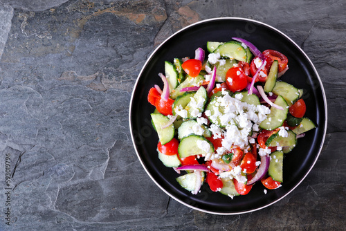 Greek salad with cucumber, tomatoes and feta cheese. Above view on a dark stone background.
