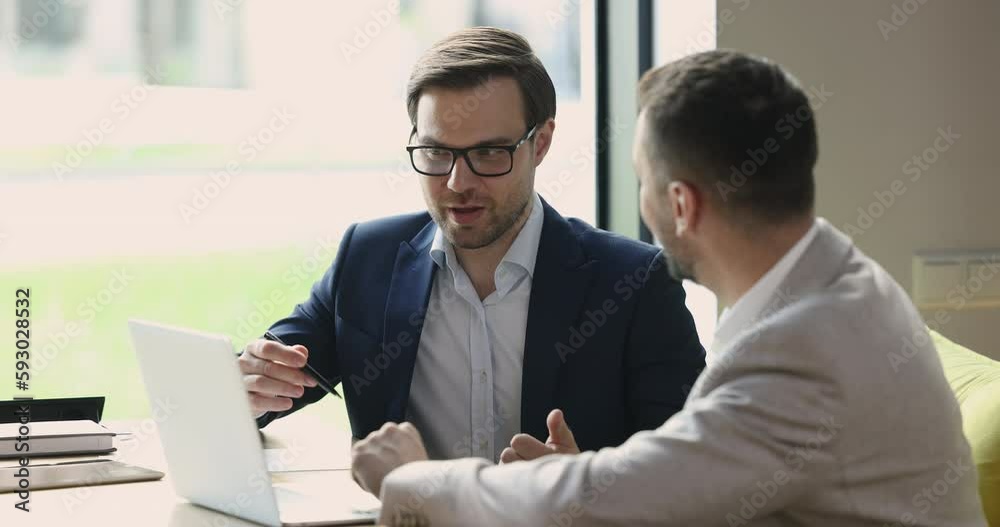 Serious confident business man telling about online project to partner, investor, speaking at open laptop. Mentor explaining listening intern work task. Manager, developer presenting software, app