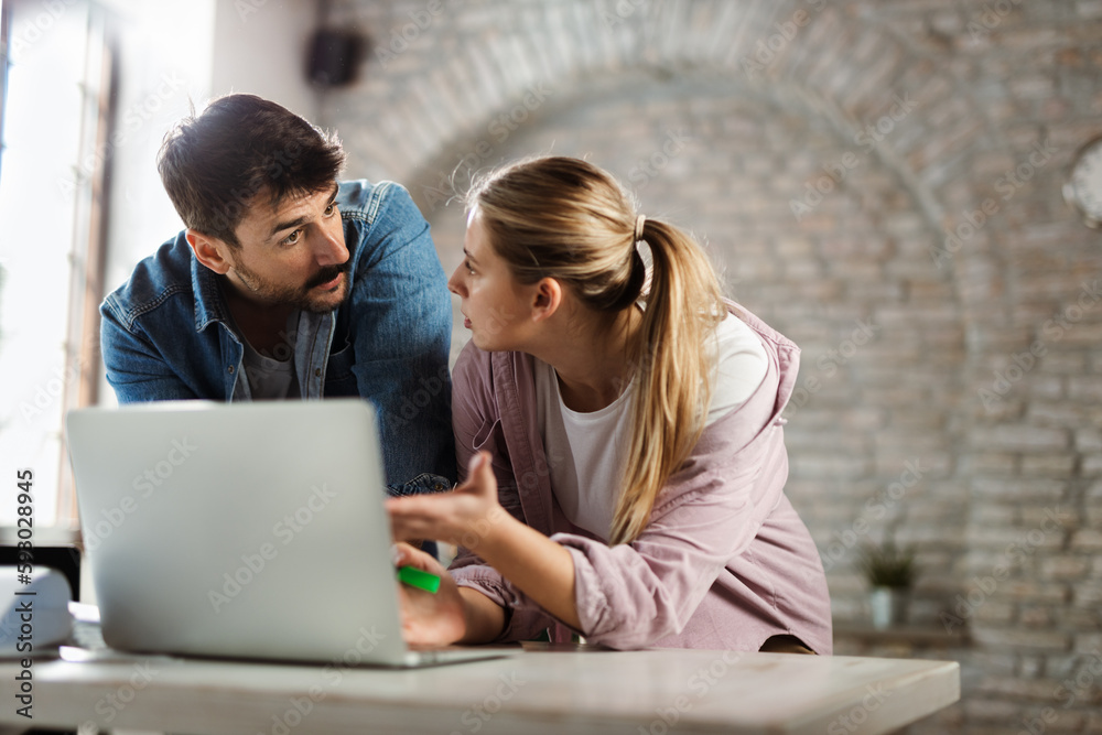 Young businessman talking to his female colleague while working on laptop in the office